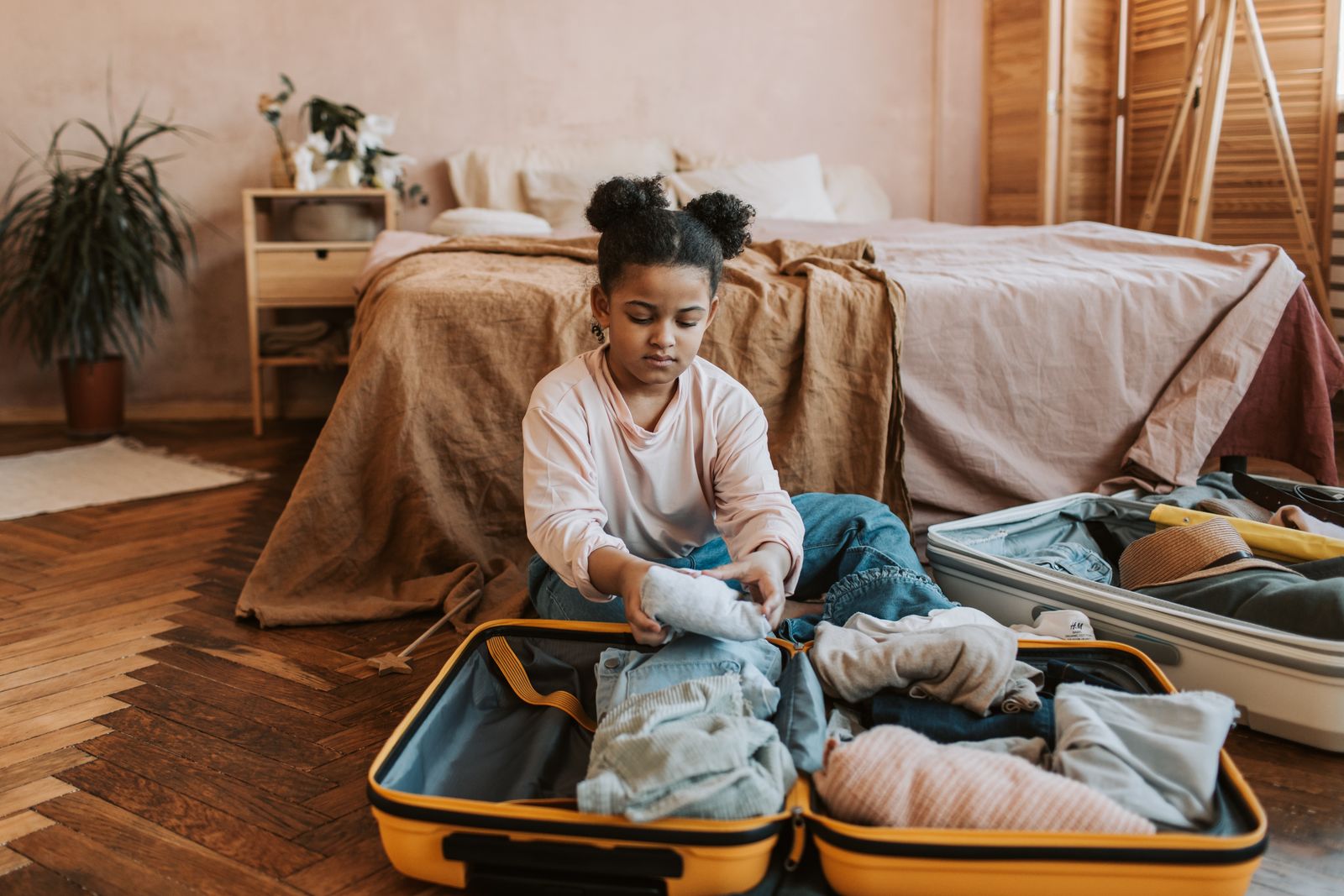 Une enfant qui prépare sa valise sur son lit, dans une chambre chaleureuse